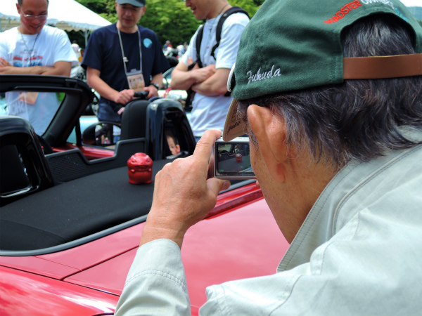 中山さんの愛車の上でNDろどすたくんを撮影する福田さん